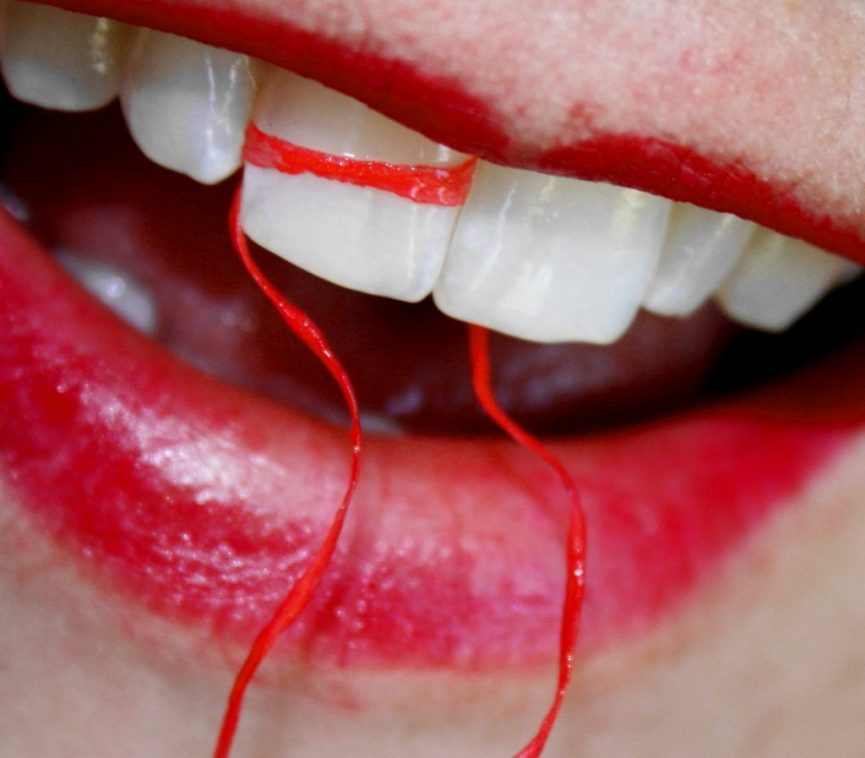 Close up of woman with red lipstick and red floss around her teeth.